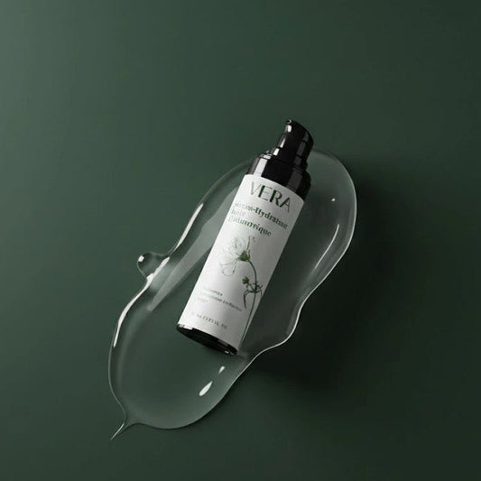 Flacon VERA du sérum hydratant à l’acide hyaluronique, en diagonale dans une goutte de gel transparent sur fond vert.