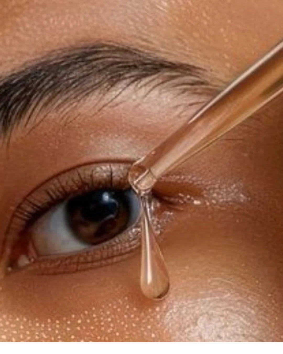 Gros plan d’un œil marron, une pipette dépose un sérum transparent près du coin externe de l’œil.