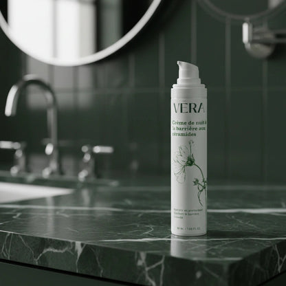 Flacon de la crème de nuit barrière aux céramides VERA sur un plan de salle de bain en marbre vert, avec miroir en arrière-plan.
