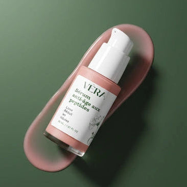 Flacon du sérum anti-âge aux peptides VERA incliné sur fond vert avec une trace de sérum.